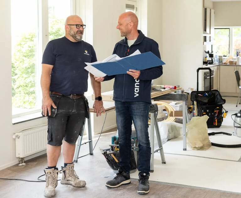 Twee mannen bespreken bouwplannen in een lichte kamer.