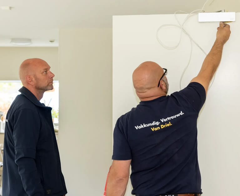 Twee mannen installeren een apparaat aan een muur