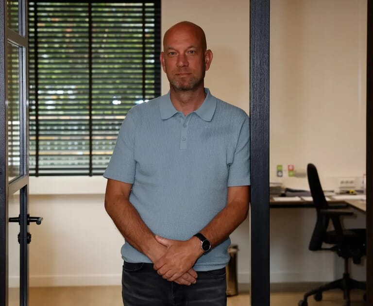 Man in blauwe polo staat in deuropening bij kantoor