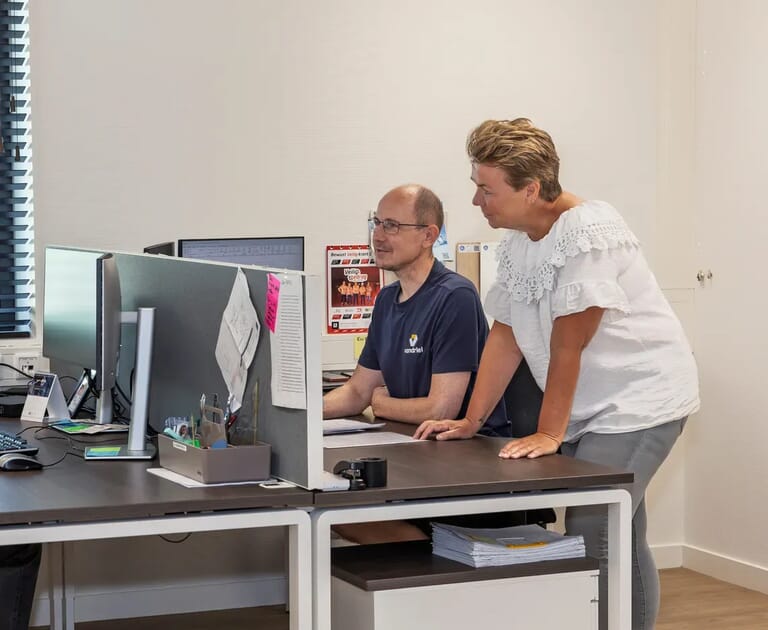 Twee mensen werken samen voor computerschermen in een kantoor.