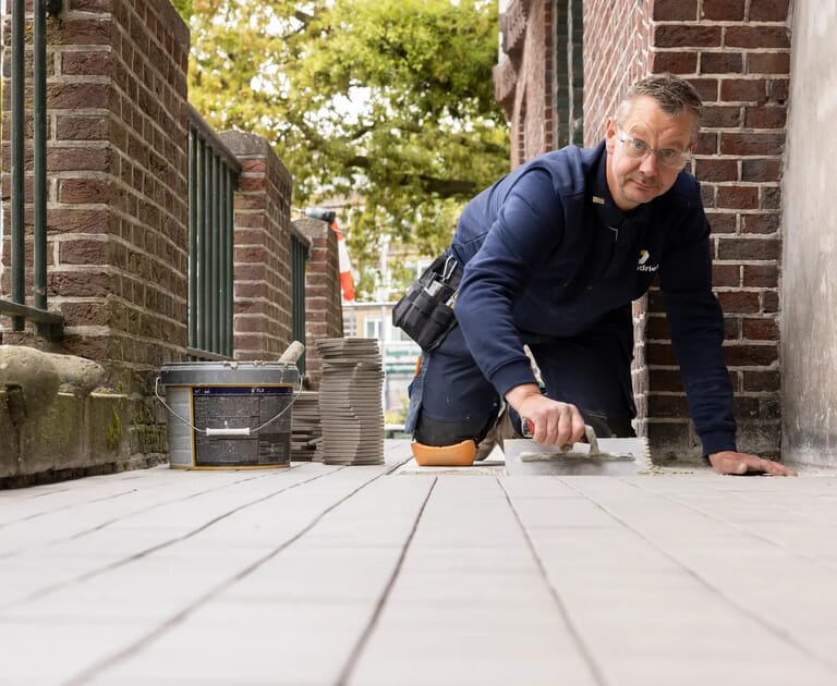Man legt vloertegels op een balkon met bakstenen muren