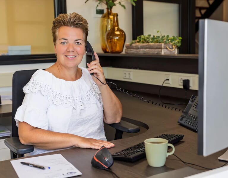 Vrouw aan bureau met telefoon en computer