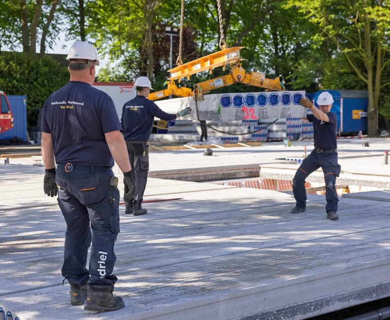 Bouwvakkers verplaatsen betonnen balk met een kraan op een bouwplaats.