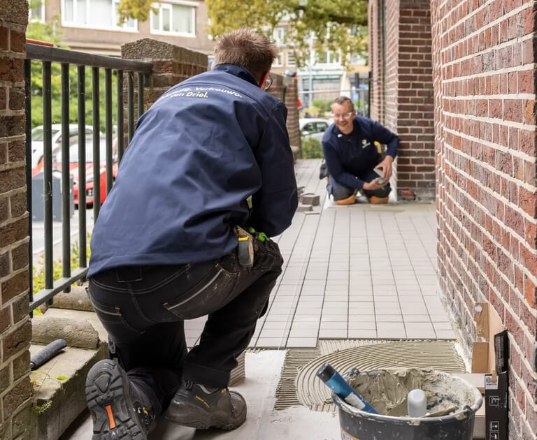 Twee mannen leggen tegels op een balkon met tegellijm.