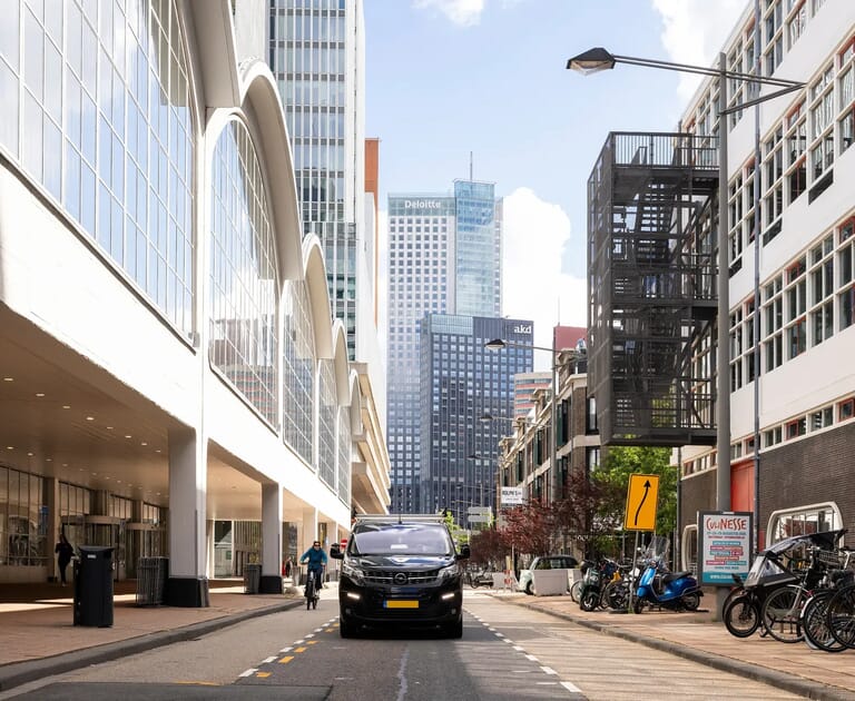 Straatbeeld met auto's, fietsers en hoge gebouwen op achtergrond.